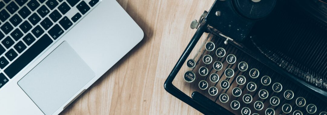 A laptop and typewriter on top of a wooden table.