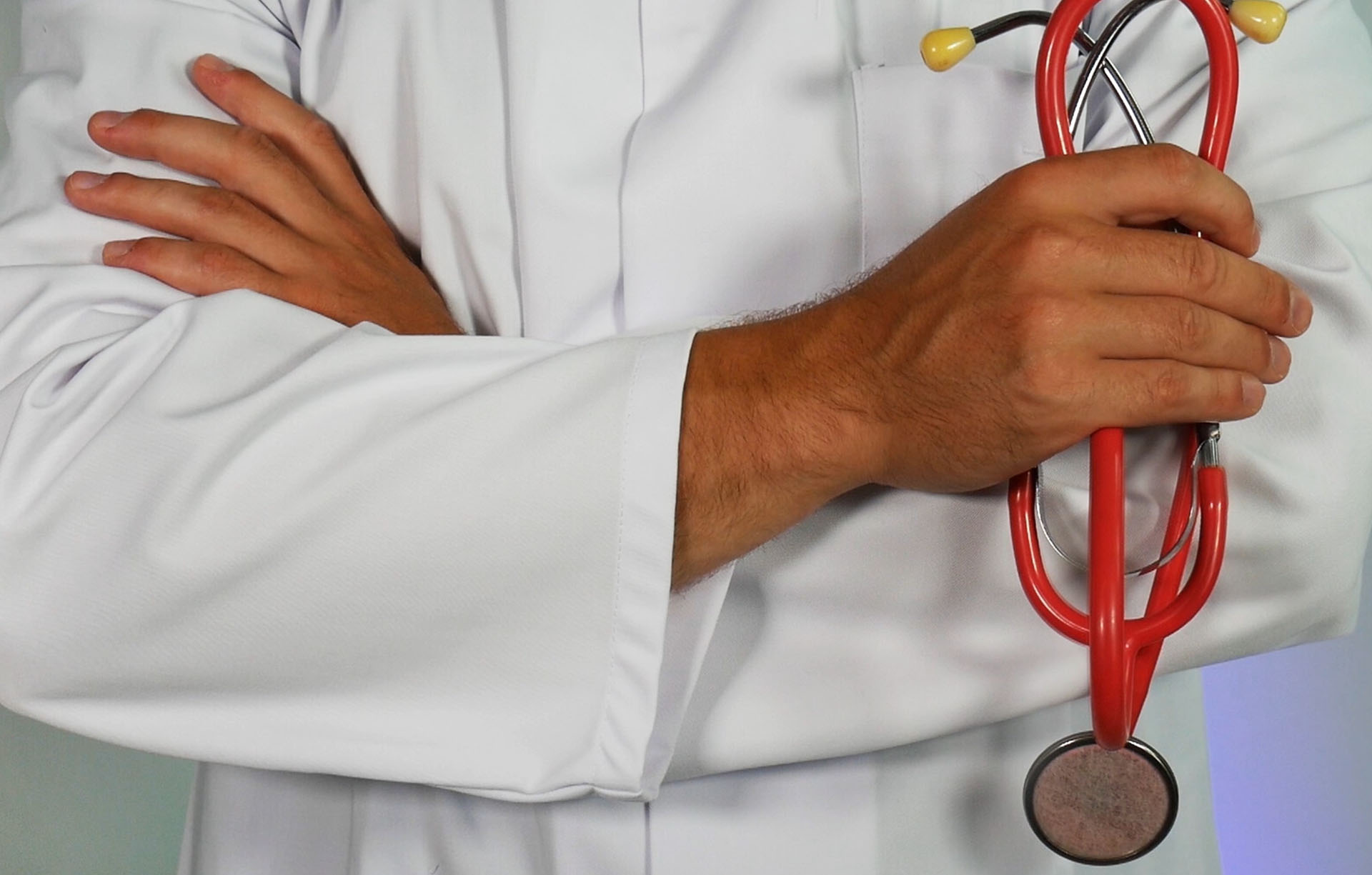 A person in white lab coat holding a red stethoscope.